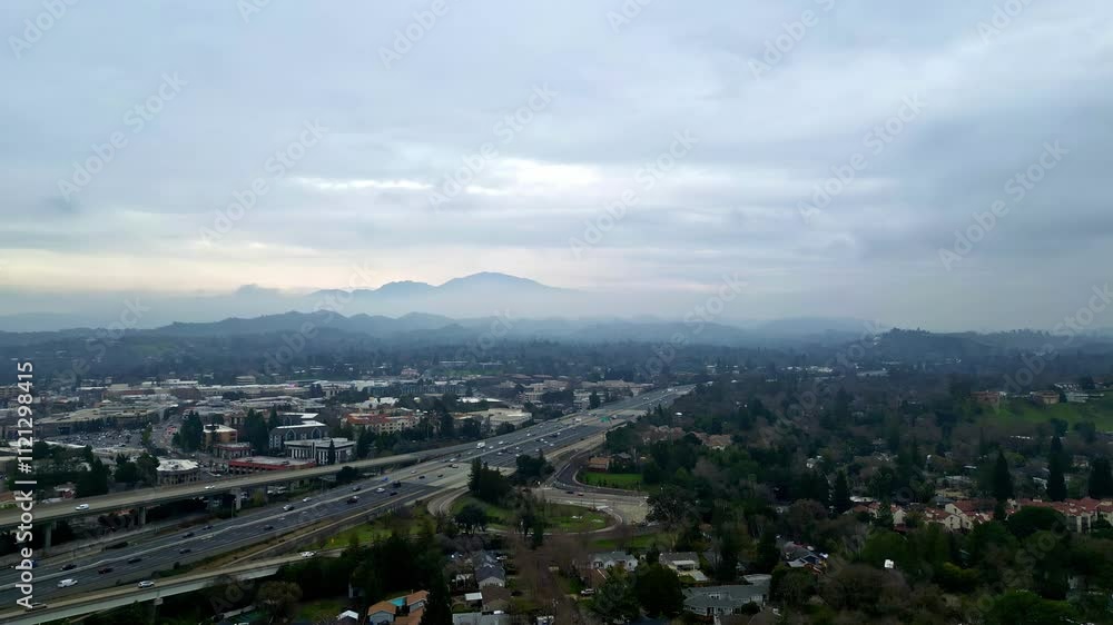 A drone captures an expansive view of a busy motorway winding through a landscape. Majestic mountains rise in the distance as dusk approaches, enhancing the serene yet dynamic atmosphere. A drone captures an expansive view of a busy motorway winding through a landscape. Majestic mountains rise in the distance as dusk approaches, enhancing the serene yet dynamic atmosphere.
