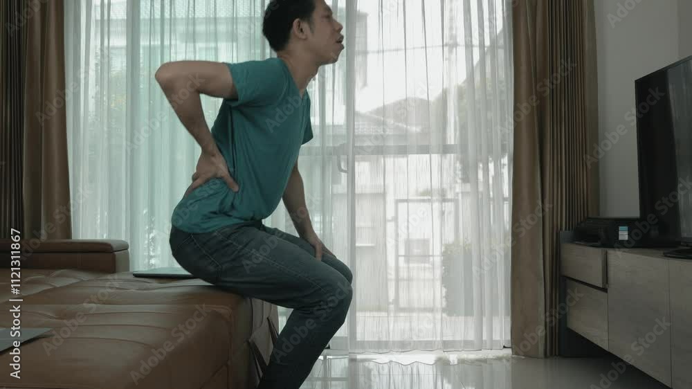 A man is sitting on a couch in a living room watching television. He is wearing a blue shirt and blue jeans A man is sitting on a couch in a living room watching television. He is wearing a blue shirt and blue jeans