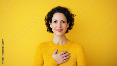 Woman touching her heart area and looking with empathy. Yellow background.