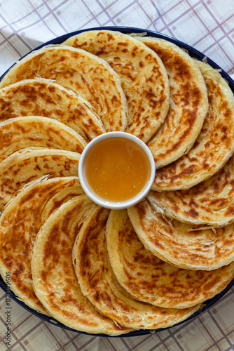 Obraz na płótnie Irregularly shaped msemen, golden and soft, served with honey on a wooden board, evoking the warmth and tradition of Moroccan breakfasts w salonie