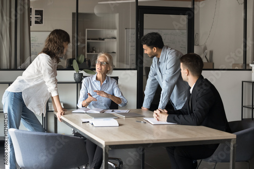 Canvas Print Middle-aged female professional business trainer hold seminar or briefing, talking to interested multiethnic trainees