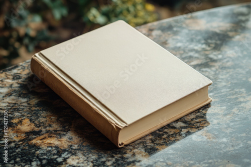 Cream-colored book with a beige cover rests on a mottled granite surface. The soft light enhances the texture and neutral tones of the scene. photo