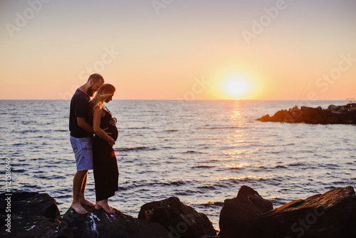 A couple, a pregnant girl and a man, at sunset by the sea