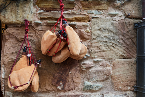 Traditional leather wine skins hanging on a rustic stone wall with red ropes in a village in Spain