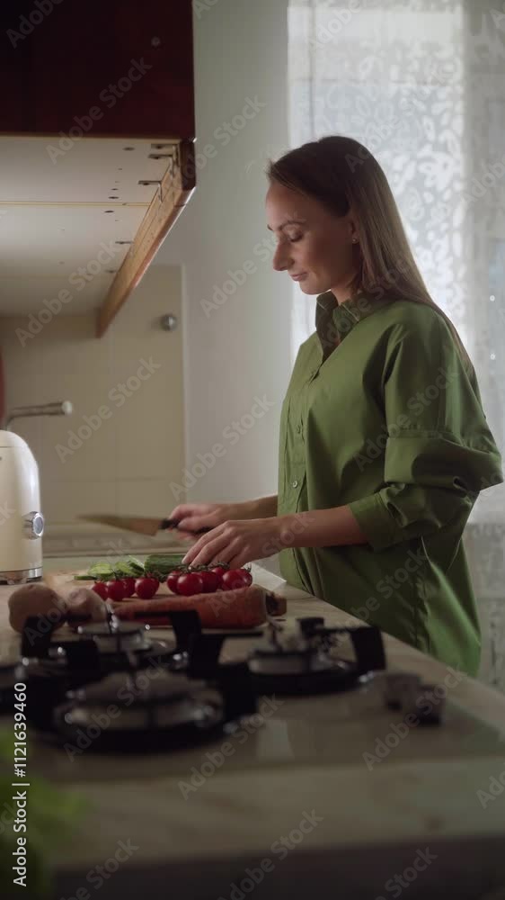 A woman prepares fresh ingredients on a countertop in a well-lit kitchen. She skillfully chops vegetables, showcasing a commitment to healthy cooking. A woman prepares fresh ingredients on a countertop in a well-lit kitchen. She skillfully chops vegetables, showcasing a commitment to healthy cooking.