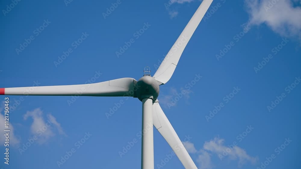 Detailed view of wind turbine with red tipped blades set against clear, vibrant blue sky on sunny day, evoking clarity and commitment to environmental sustainability