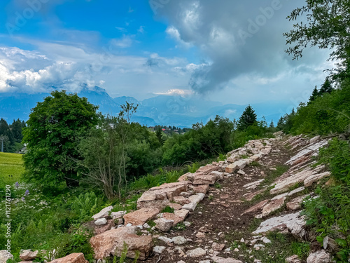 Scenic hiking trail towards mountain peak Palon in Garda Prealps, Trentino Alto Adige, Italy. Looking at cloud covered distant summit of Paganella in Brenta Dolomites. Wanderlust in Verson near Trento photo