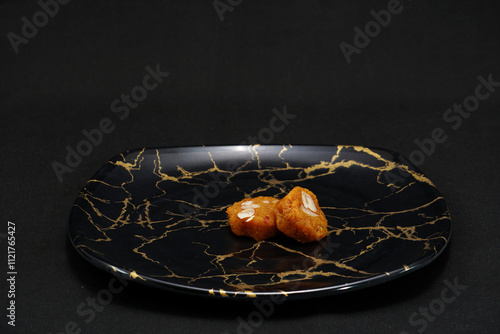 A black plate holds two pieces of the traditional Gujarati sweet known as Mohanthal photo