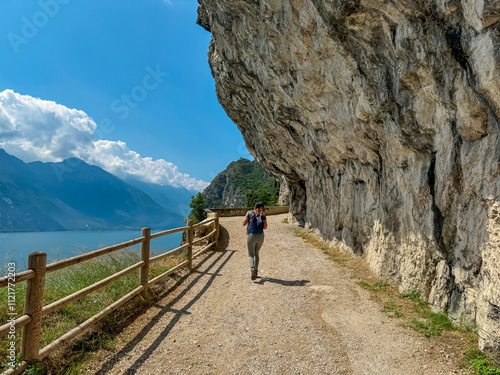 Obraz na płótnie Hiker woman on hiking trail Sentiero del Ponale with scenic view of Garda Lake, Trentino, Northern Italy. Steep rugged cliffs of majestic mountains of Garda Hills. Summer travel vacation, Italian Alps w salonie