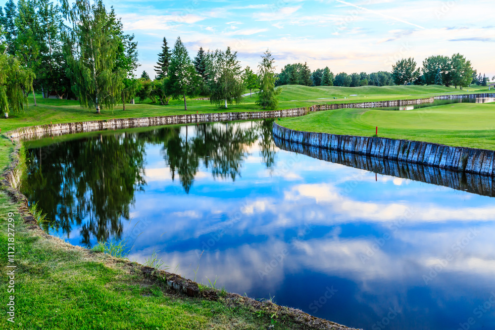 Obraz premium A body of water with a green grassy bank and trees in the background