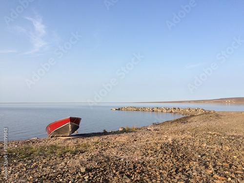 A lonely red metal boat on a a rocky shoreline with blues skies. Baker Lake, Nunavut