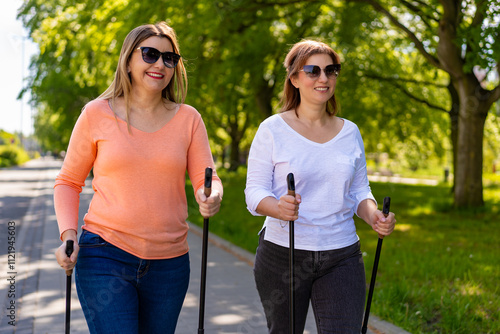 Nordic walking - two mature beautiful women exercising in city park using Nordic walking poles. Portrait photo