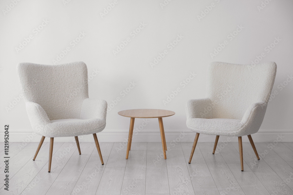 Fototapeta premium Soft armchairs and coffee table near white wall indoors