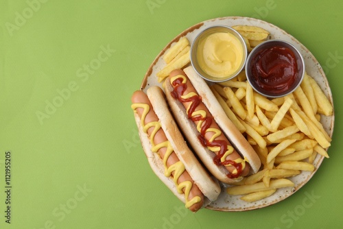 Photography Tasty hot dogs with fries and sauces on green background, top view