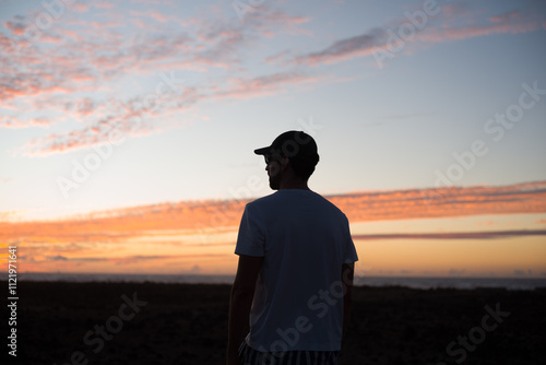 Silueta de hombre con gorramirando los colores dorados del cielo al atardecer en la costa en verano