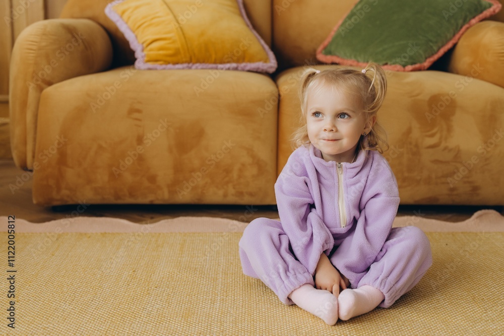 Smiling toddler wearing purple jumpsuit sitting on carpet in living room Smiling toddler wearing purple jumpsuit sitting on carpet in living room