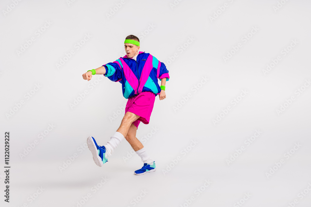 Fototapeta premium Young man in colorful retro activewear energetically performing a dynamic exercise on a white background
