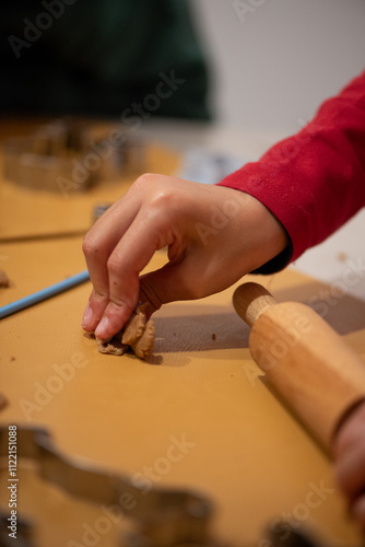 detail of girl's hands kneading christmas biscuits, red clothes colours, lighted candle with centre in front of it