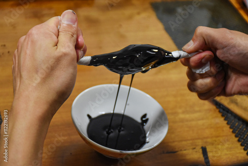 Hands filter the black Japanese raw lacquer, Urushi, through a fine cloth, squeezing out impurities. The process emphasises precision and tradition, and brings out the lustrous purity of the lacquer. photo