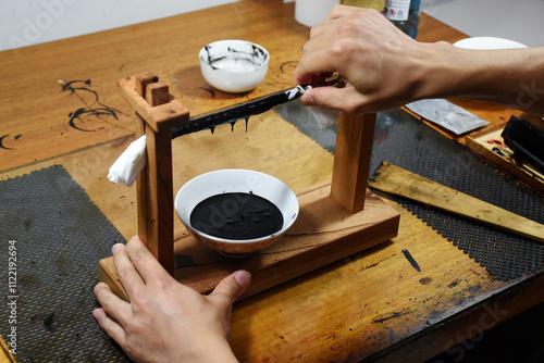 Hands filter the black Japanese raw lacquer, Urushi, through a fine cloth, squeezing out impurities. The process emphasises precision and tradition, and brings out the lustrous purity of the lacquer. photo