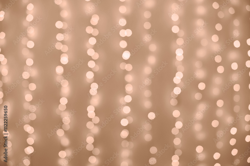 Fototapeta premium Defocused shiny light garlands hanging on wall and illuminating cozy room in evening at home. Demonstrating Mocha and Mousse color of 2025 year