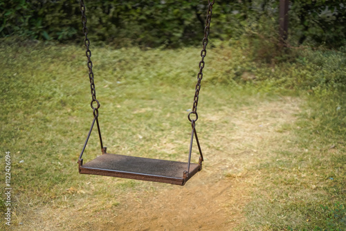 Empty Swing in Garden, Rustic Swing Set, Vintage Playground Swing, Solitary Swing in Park, Swing with Greenery Background, Old Swing Outdoors, Peaceful Park Swing. 

 photo