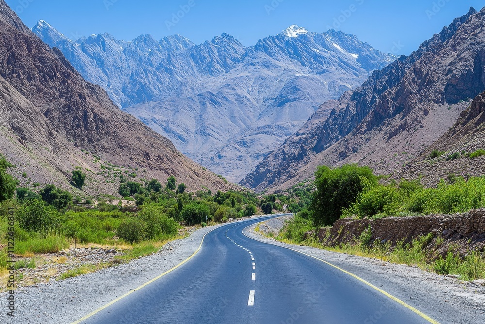 Naklejka premium Asphalt road winds through a valley, majestic mountains in the background. Ideal for travel, adventure, and nature-themed projects.