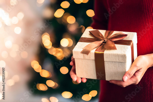 Hand of woman offer gift box to lovers on christmas tree light background. have a copy space for text. Close up on woman hands giving Christmas present. Christmas gift.