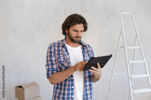 Focused man in a plaid shirt using a tablet to plan a DIY home renovation project. Ideal for concepts related to home improvement, interior design, and project management.  photo