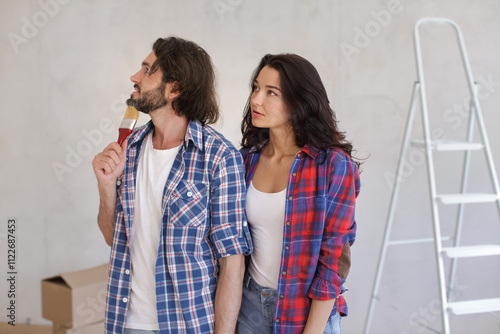 Pensive couple holding a paintbrush and looking thoughtful, planning a DIY home renovation project. Ideal for concepts related to home improvement, interior design, and creative projects.  photo