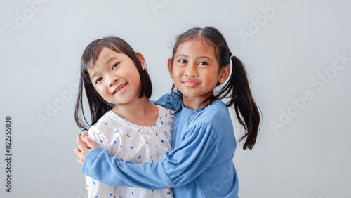 Studio portrait of Asian children on a light background, two children hugging as a best friend and smiling to the camera.