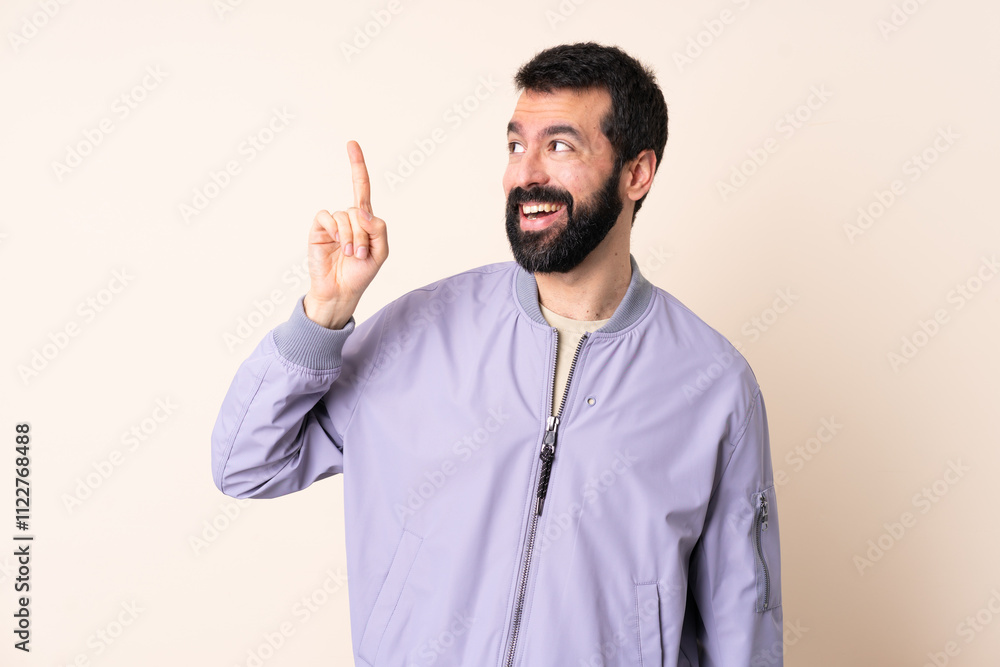 Naklejka premium Caucasian man with beard wearing a jacket over isolated background intending to realizes the solution while lifting a finger up