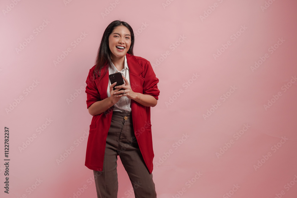Naklejka premium Excited young Asian woman in a red jacket is holding smartphone with smiling expression.
