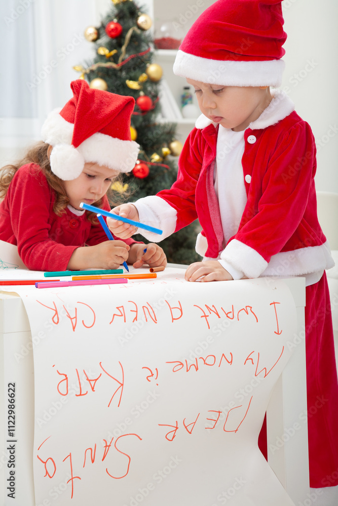 little kids in Santa hat writing letter to Santat under the Christmas tree