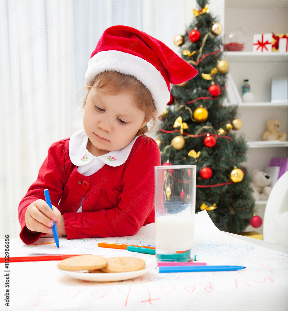 little girl in Santa hat writing letter to Santat under the Christmas tree