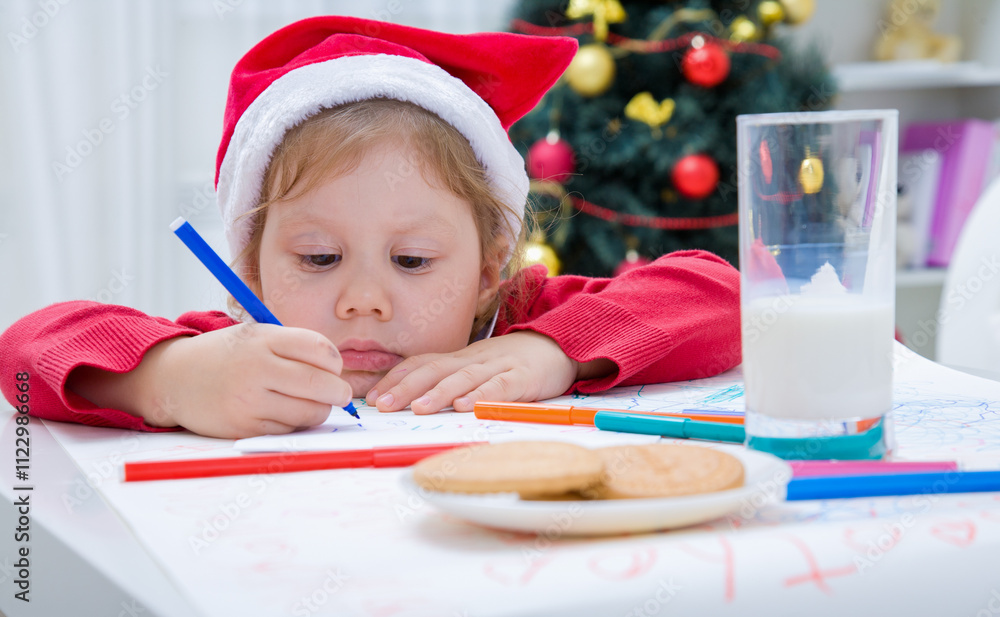 little girl in Santa hat writing letter to Santat under the Christmas tree