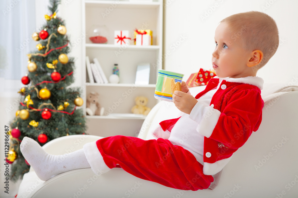 Portrait of little cute boy in Santa hat drinking milk with biscuit