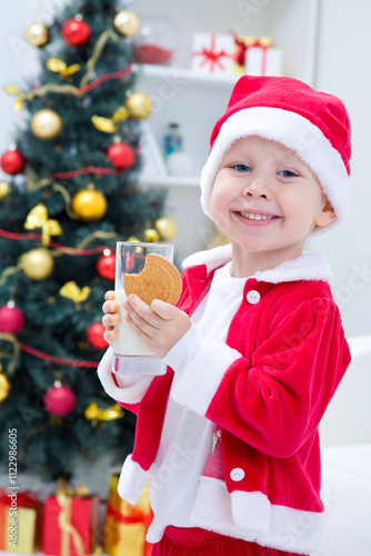 Obraz na płótnie Portrait of little cute boy in Santa hat drinking milk with biscuit w salonie