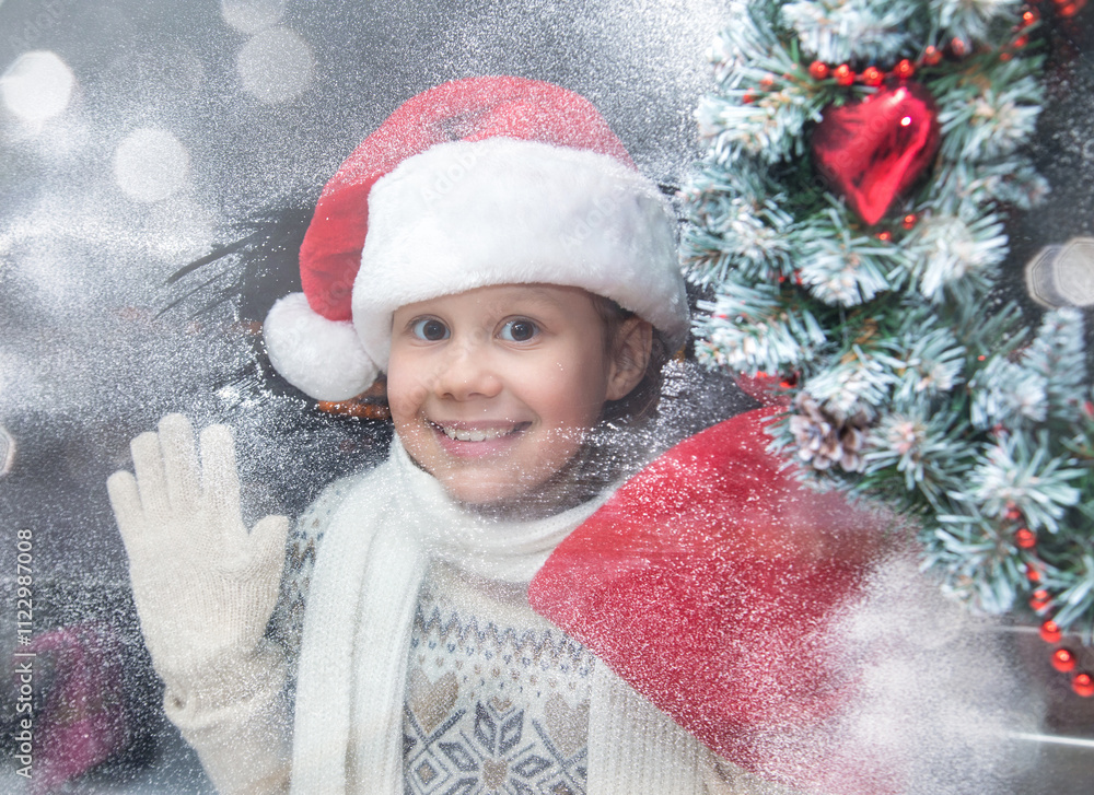little girl in santa hat and with gifts shines a lantern into the window from winter street