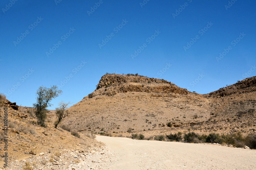 Dirt road between desert hills against a blue sky. Desert landscape and environment Dirt road between desert hills against a blue sky. Desert landscape and environment