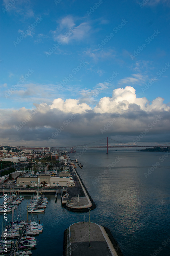 Obraz premium Lisbon cityscape with 25 de abril bridge over tagus river under cloudy sky