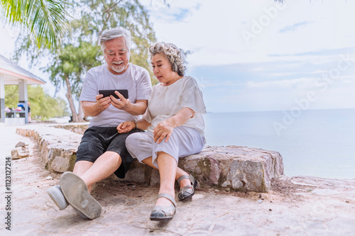 Obraz na płótnie Happy asian senior retired couple; relax elder man and woman enjoying with smartphone apps, middle-aged wife enjoy online entertainments in retired vacation at sea beach outdoor. w salonie