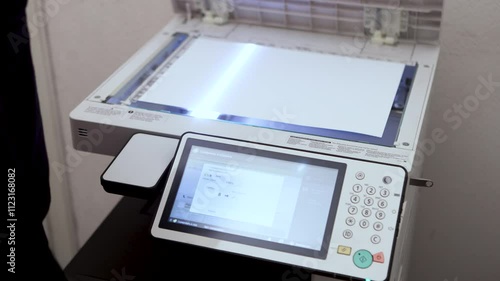 An office worker scans an A3 sheet of paper on a scanner. A man's hand presses a button to scan or copy a document on an office MFP.