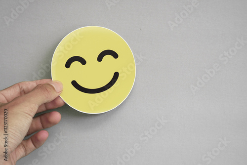 Hands holding a happy smiling face in yellow.