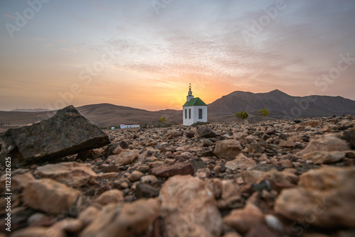 small cute white wooden chapel in a barren volcanic landscape. Sunrise, landscape shot of Ermita Protestante de Violante church, on Fuerteventura island, Canary Islands, Spain photo