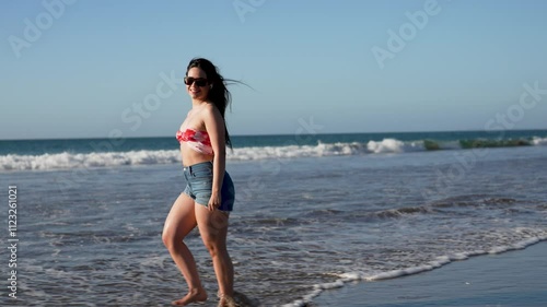Beautiful latin woman walking on the beach and listening to music, summer and vacation concept
