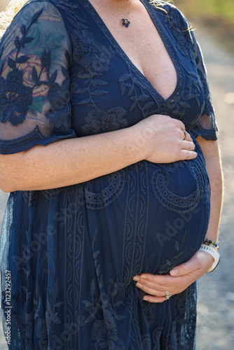 Pregnant woman cradles baby bump belly wearing blue dress for expecting mother surrogacy