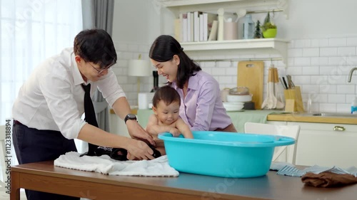 Asian baby taking a bath in a blue tub at home.