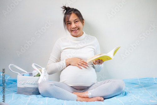 pregnant woman reading book while sitting on bed, surrounded by baby items. She looks happy and relaxed, enjoying her time preparing for motherhood