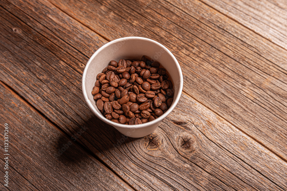 Coffee beans in a paper cup on a wooden background.